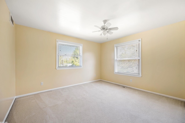 carpeted spare room with baseboards, ceiling fan, and visible vents