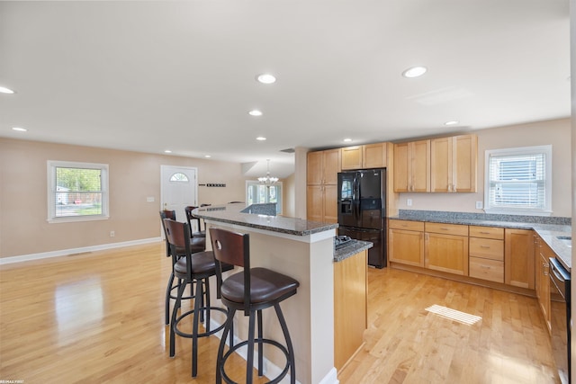 kitchen featuring black refrigerator with ice dispenser, a breakfast bar, and light wood finished floors