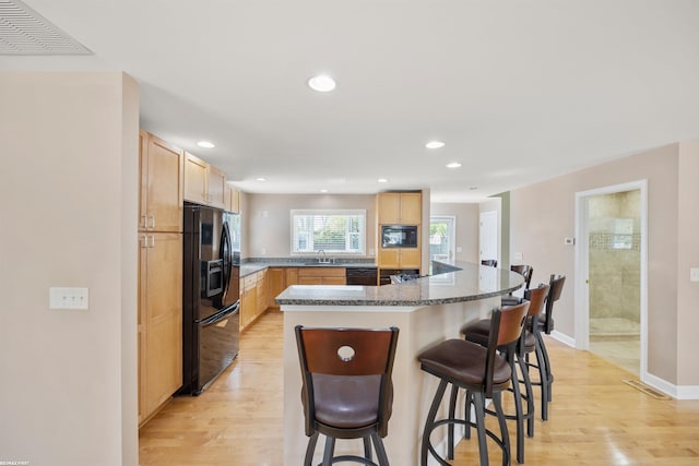 kitchen with light wood-style floors, light brown cabinetry, black appliances, and visible vents