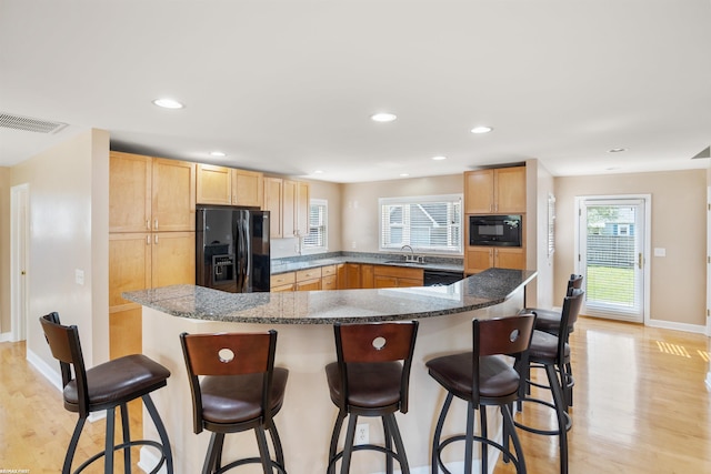 kitchen with light brown cabinets, a wealth of natural light, light wood-style floors, a sink, and black appliances