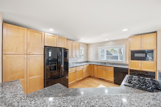 kitchen with light brown cabinetry, light stone countertops, light wood-type flooring, a sink, and black appliances