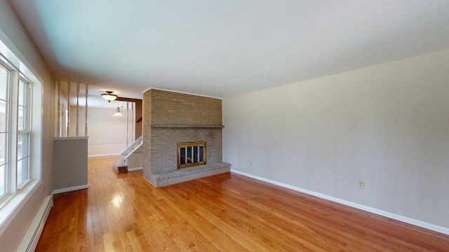 unfurnished living room with a fireplace, baseboards, baseboard heating, and light wood-style floors