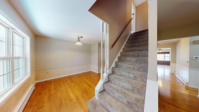 stairway with a baseboard radiator, wainscoting, and wood finished floors