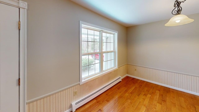 empty room featuring light wood-type flooring, a baseboard heating unit, and a wainscoted wall