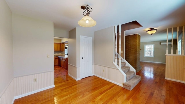 empty room with light wood finished floors, wainscoting, and stairway