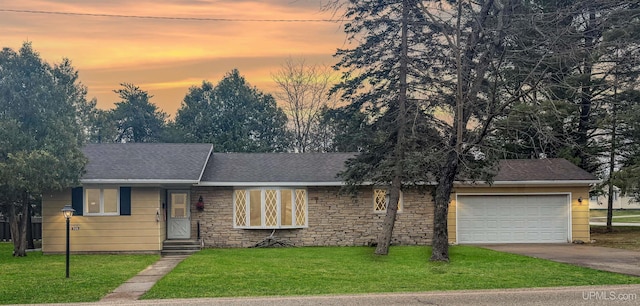 view of front facade featuring stone siding, a shingled roof, concrete driveway, an attached garage, and a yard