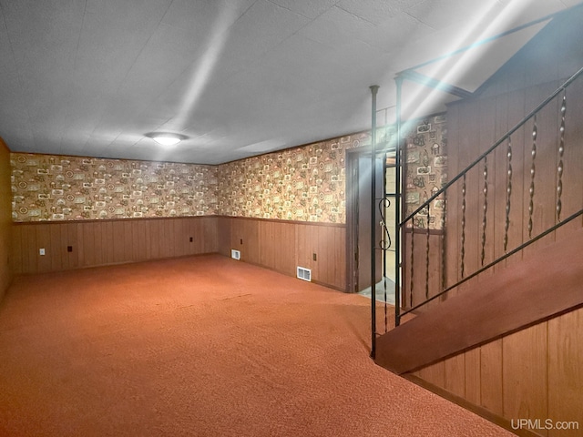 finished basement with stairs, visible vents, carpet, and a wainscoted wall