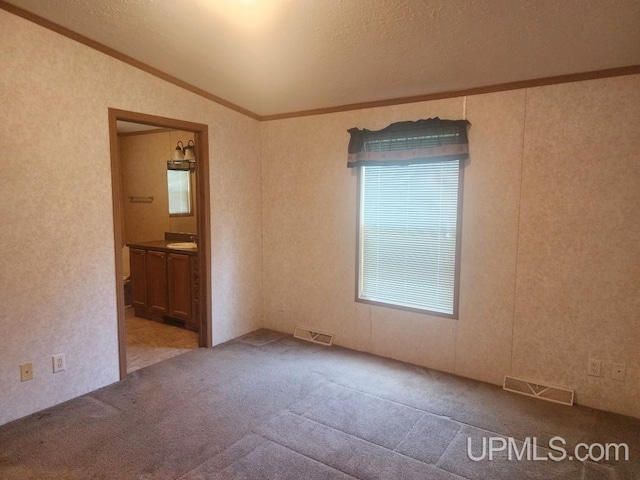 carpeted spare room featuring visible vents, ornamental molding, a textured ceiling, and lofted ceiling