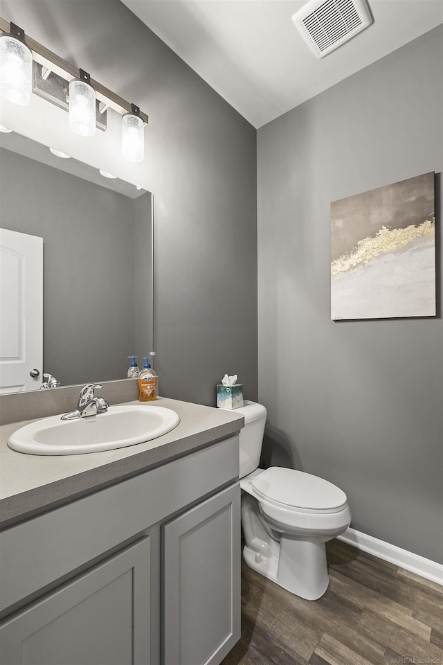 half bathroom featuring visible vents, vanity, wood finished floors, toilet, and baseboards