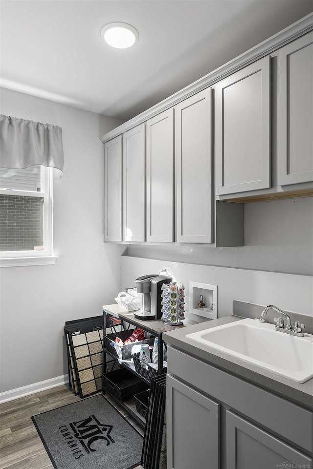 laundry area featuring cabinet space, washer hookup, a sink, baseboards, and wood finished floors