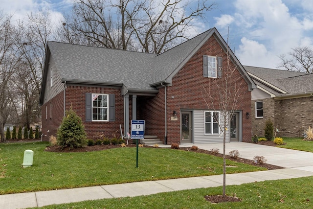 traditional home with concrete driveway, brick siding, a front yard, and roof with shingles