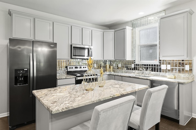 kitchen featuring a sink, appliances with stainless steel finishes, a center island, and light stone counters