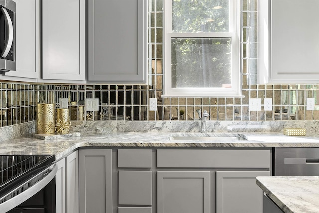 kitchen with a sink, appliances with stainless steel finishes, tasteful backsplash, and light stone counters
