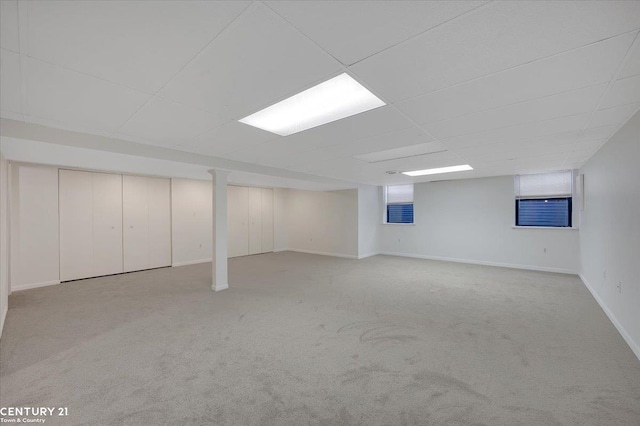 finished basement with carpet floors, baseboards, and a paneled ceiling