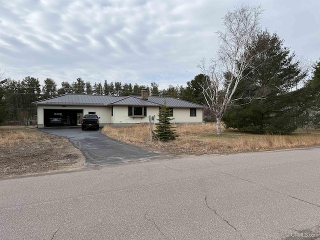 ranch-style house with a garage, a chimney, driveway, and metal roof