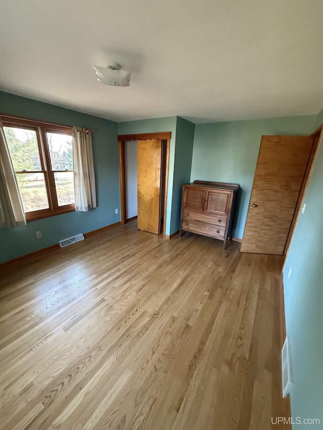 unfurnished bedroom featuring baseboards, a closet, wood finished floors, and visible vents
