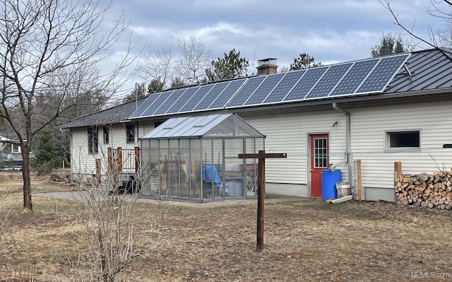 rear view of house with roof mounted solar panels, an outdoor structure, a chimney, and an exterior structure