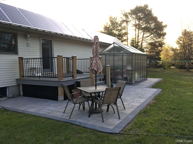 patio terrace at dusk with an outbuilding, a yard, a greenhouse, and a deck