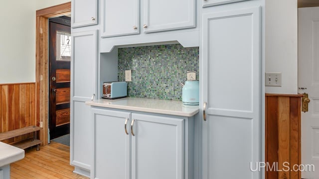 kitchen with wainscoting, light wood-style floors, light countertops, white cabinetry, and tasteful backsplash