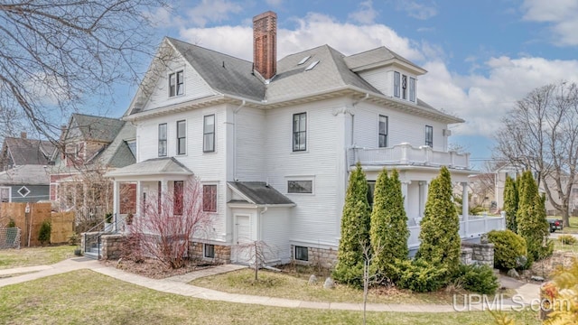 view of side of property featuring fence, roof with shingles, a chimney, a balcony, and a yard