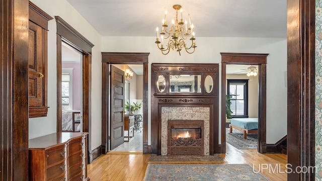 interior space featuring light wood-style floors, baseboards, ceiling fan with notable chandelier, and a tile fireplace