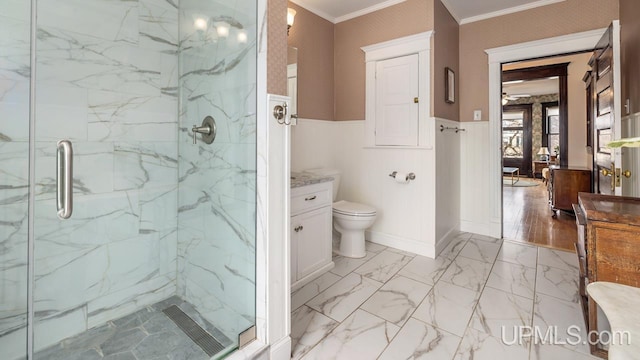bathroom featuring wainscoting, vanity, toilet, a marble finish shower, and ornamental molding