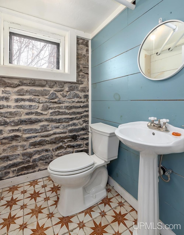 half bathroom featuring toilet, tile patterned floors, wood walls, and a sink