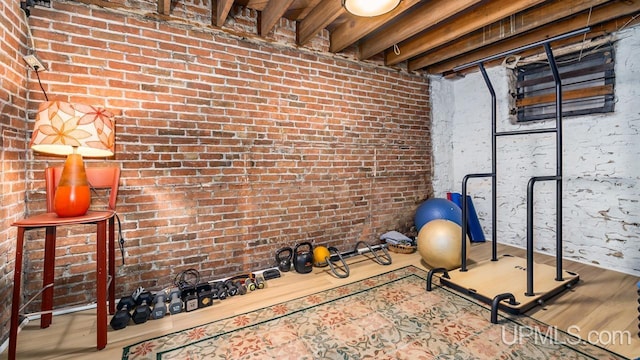 exercise room featuring brick wall and wood finished floors