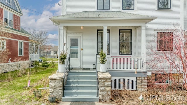 entrance to property featuring covered porch and roof with shingles
