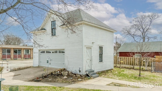 view of side of property featuring fence, roof with shingles, an attached garage, entry steps, and concrete driveway