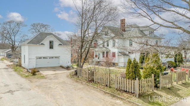 view of side of property featuring a garage, dirt driveway, fence, and a chimney