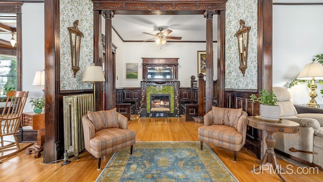 sitting room featuring radiator heating unit, a wainscoted wall, a ceiling fan, wood finished floors, and a high end fireplace