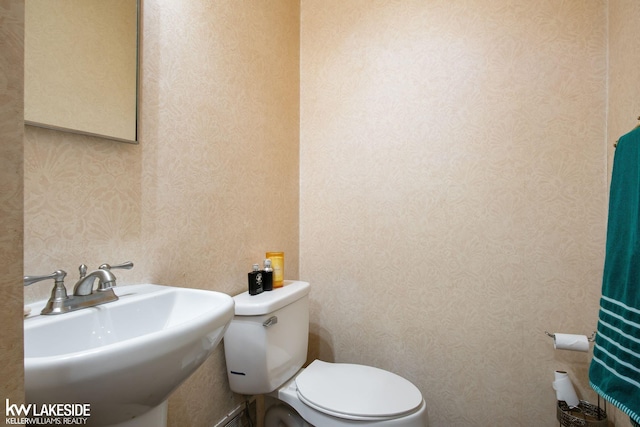 half bathroom featuring a sink, wallpapered walls, and toilet