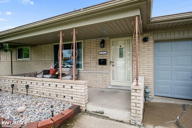 property entrance with covered porch, brick siding, and a garage