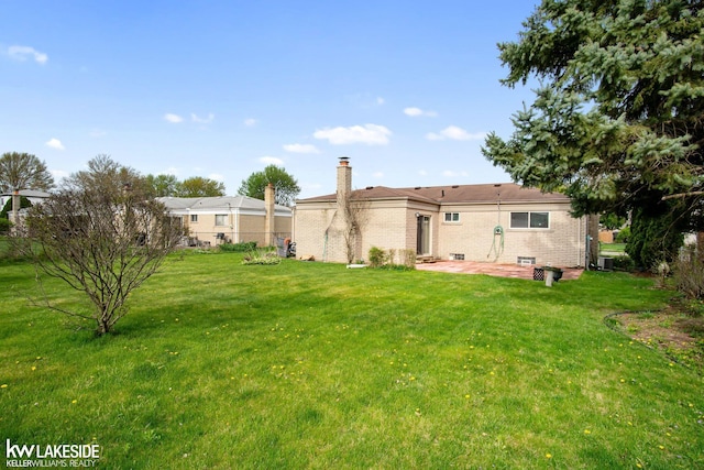 rear view of property with a yard, brick siding, a chimney, and a patio area