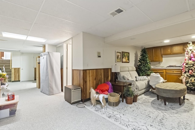 living room featuring visible vents, a wainscoted wall, wooden walls, light carpet, and a drop ceiling