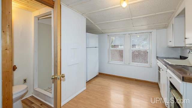interior space featuring freestanding refrigerator, white cabinets, and light wood-style flooring