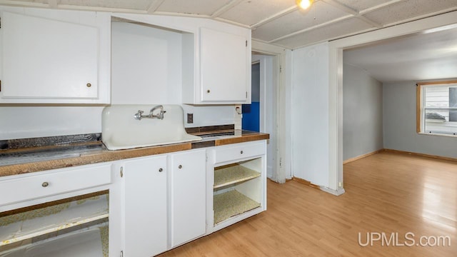 kitchen featuring dark countertops, a sink, baseboards, light wood finished floors, and white cabinetry