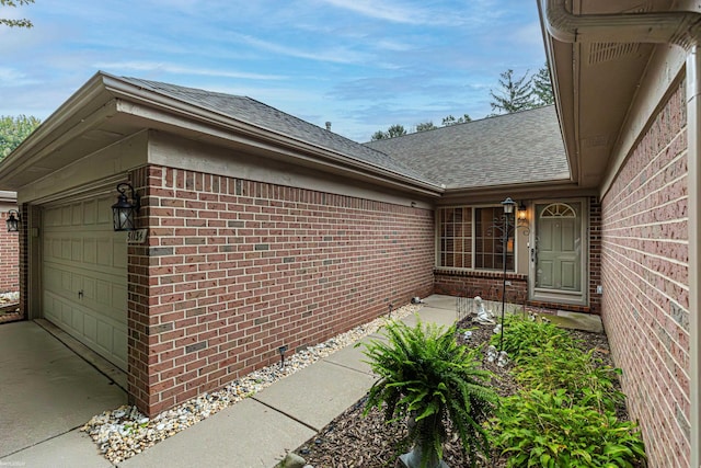 entrance to property with roof with shingles, a garage, and brick siding