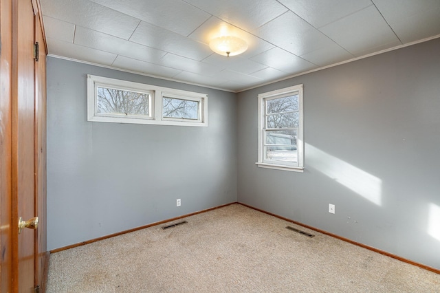 carpeted spare room featuring crown molding, baseboards, and visible vents