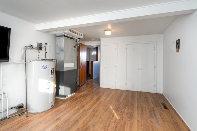 below grade area featuring visible vents, heating unit, light wood-style floors, and water heater