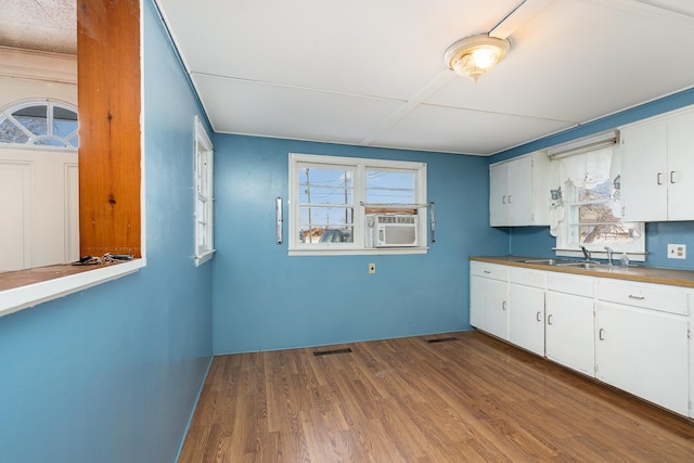 kitchen with a sink, white cabinets, dark wood-style floors, and visible vents