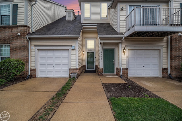townhome / multi-family property with a shingled roof, driveway, brick siding, and a balcony