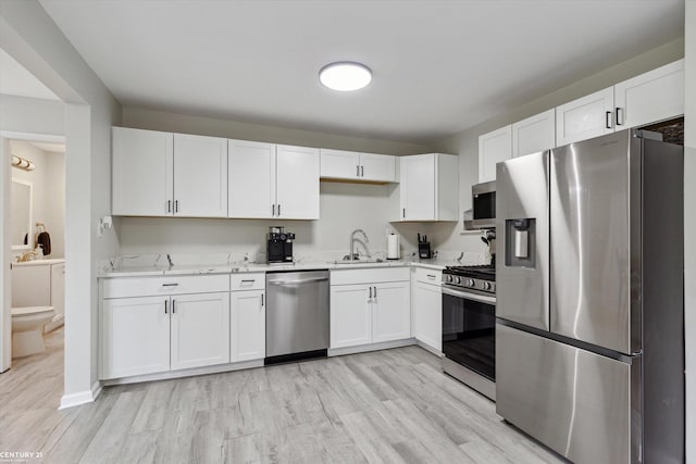 kitchen featuring a sink, white cabinets, stainless steel appliances, and light wood-type flooring