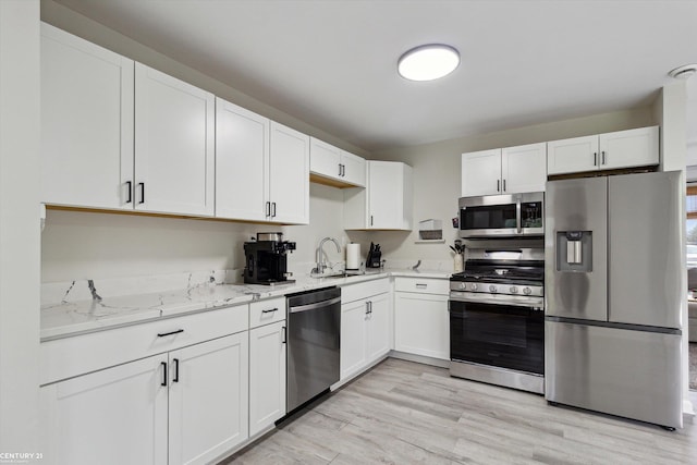 kitchen featuring white cabinets, light stone counters, a sink, light wood-style floors, and stainless steel appliances
