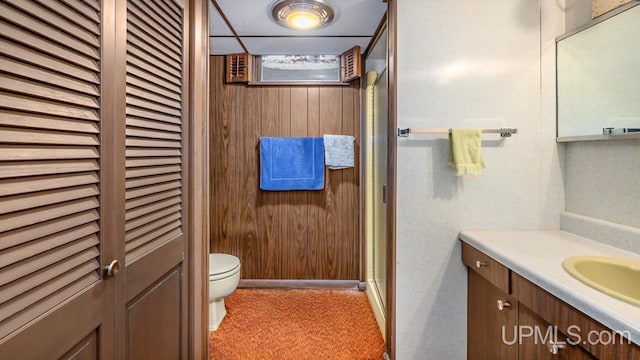 bathroom with vanity, toilet, wood walls, a closet, and a stall shower