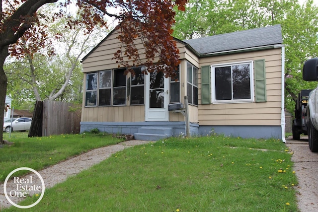 bungalow-style home with roof with shingles, fence, and a front yard