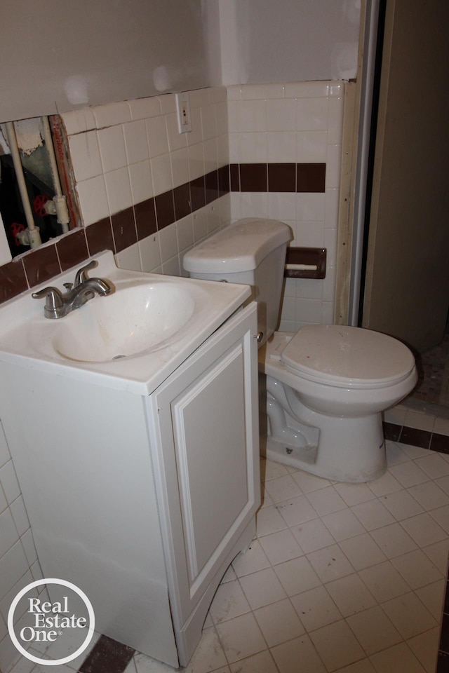 half bathroom featuring tile walls, tile patterned floors, vanity, and toilet