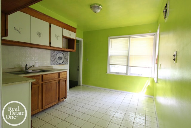 kitchen featuring light tile patterned flooring, a sink, light countertops, baseboards, and tasteful backsplash