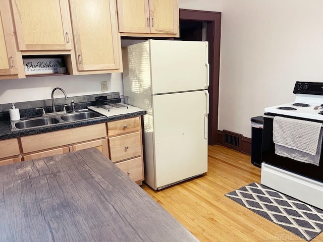 kitchen featuring dark countertops, a sink, light brown cabinets, white appliances, and visible vents
